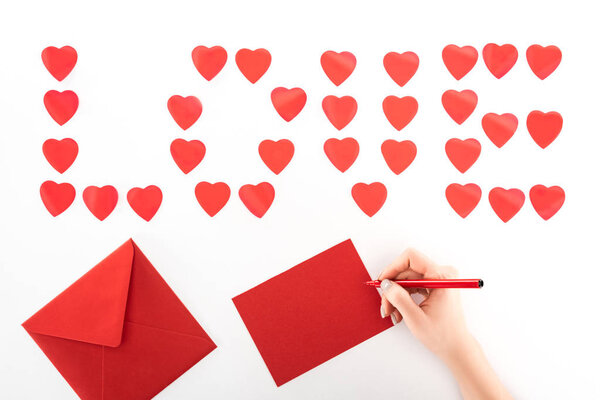 partial view of woman writing greeting card under lettering love made of red heart symbols isolated on white, st valentine day concept