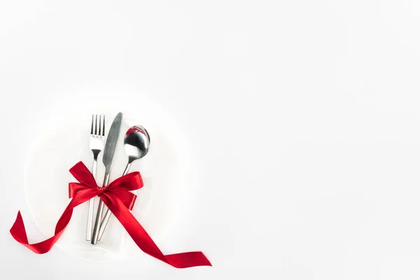 Elevated view of fork, knife and spoon wrapped by red festive bow on plate isolated on white, st valentine day concept — Stock Image Elevated View Fork Knife Spoon Wrapped Red Festive Bow Plate Royalty Free Stock Images