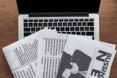 top view of newspapers and laptop on wooden tabletop clipart
