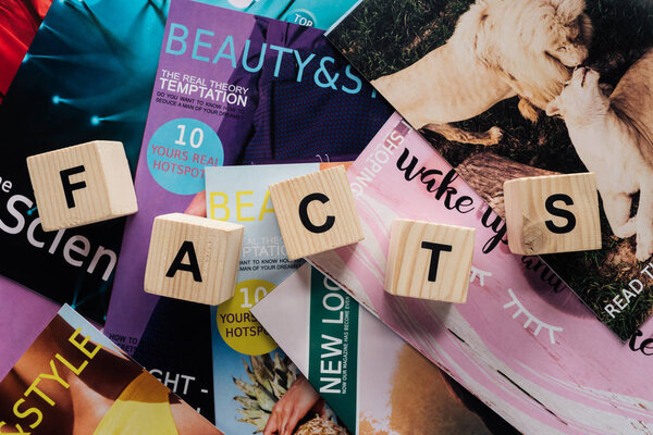 top view of pile of different tabloid magazines and wooden cubes with word facts on surface