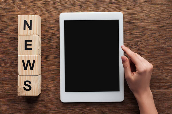 cropped image of journalist using tablet with blank screen, wooden cubes with word news on wooden table