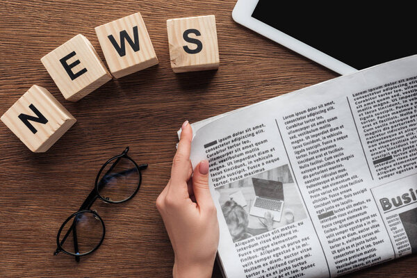 cropped image of journalist holding newspaper, wooden cubes with word news at wooden table