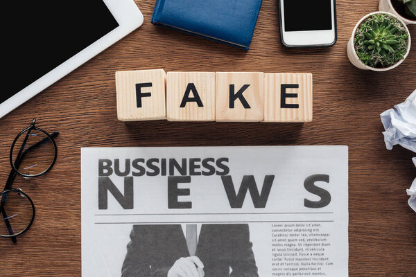 top view of wooden cubes with word fake and business newspaper on wooden tabletop