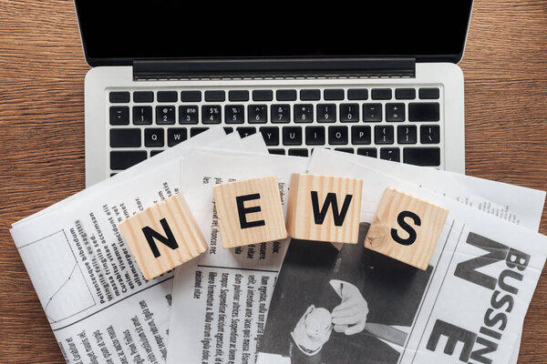 top view of wooden cubes with word news and newspapers on laptop on wooden tabletop