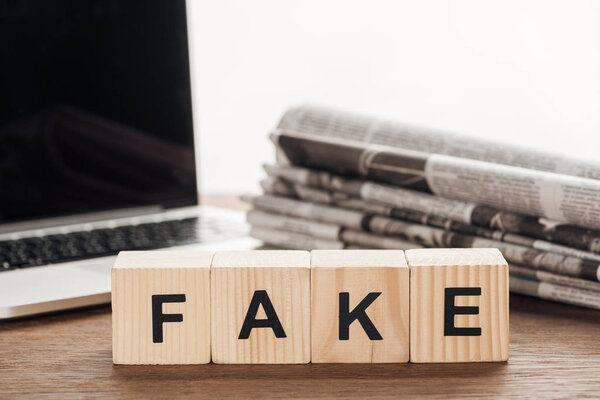 wooden cubes with word fake, laptop and newspapers on wooden tabletop