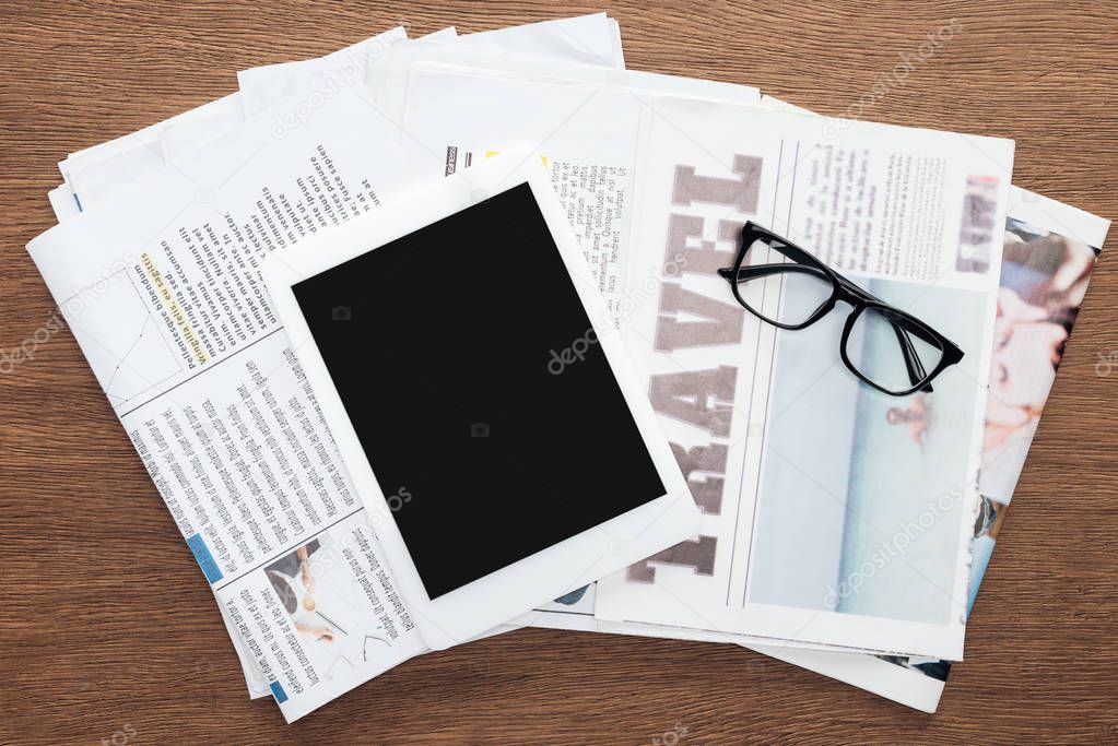 top view of tablet with blank screen, glasses and newspapers on wooden tabletop