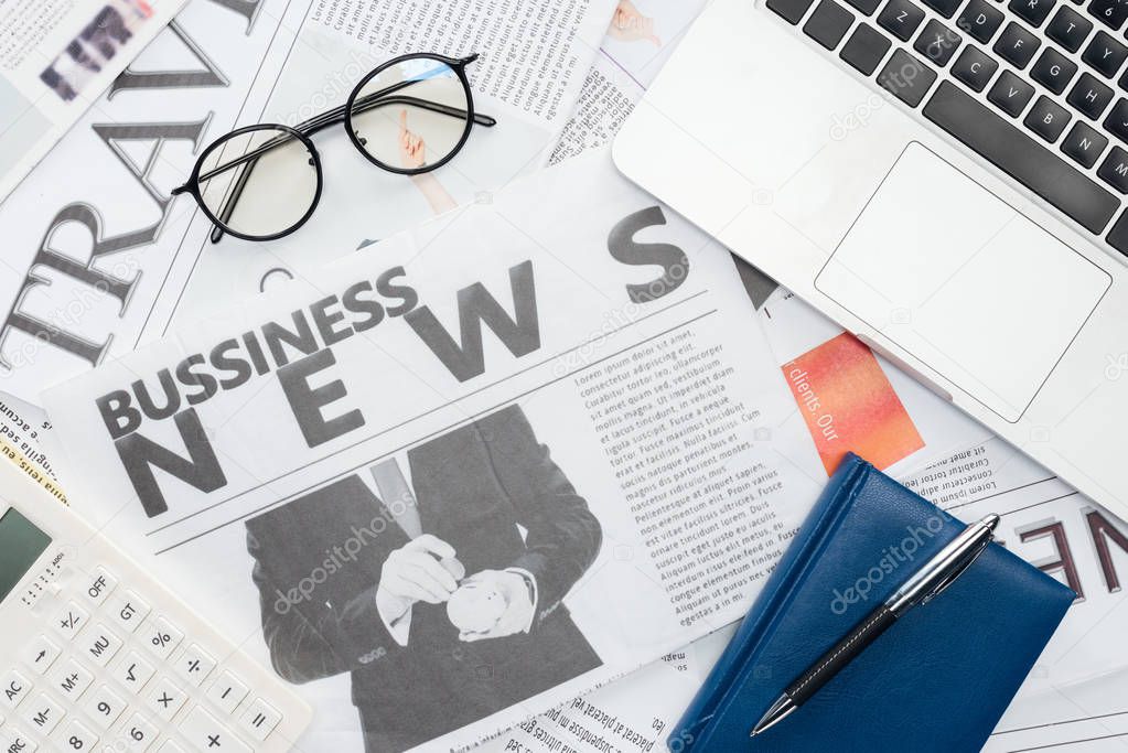 top view of eyeglasses, pen and notebook and laptop on newspapers