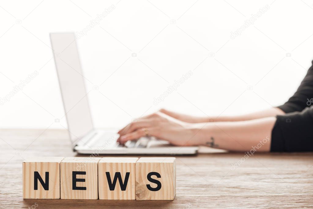 cropped image of journalist working at laptop, wooden cubes with word news on tabletop