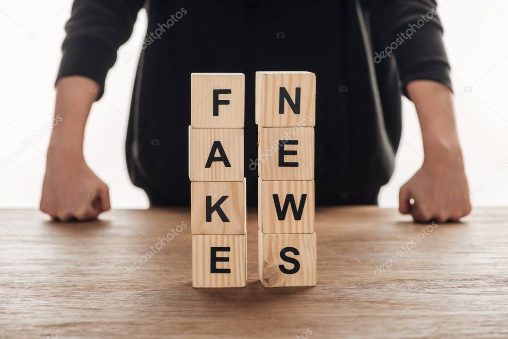 cropped image of journalist leaning on tabletop with wooden cubes with words fake news