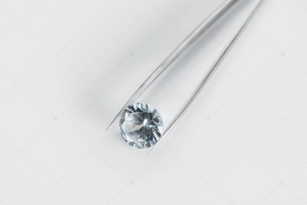 top view of shiny diamond in tweezers on white background