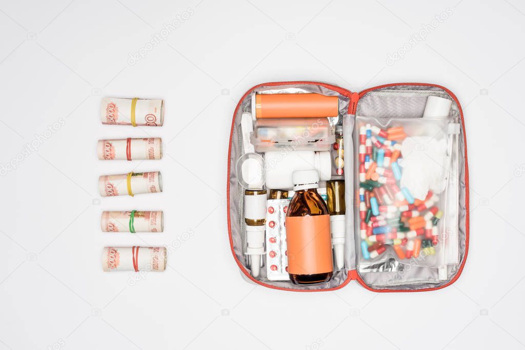 top view of money rolls and first aid kit with medicine isolated on grey