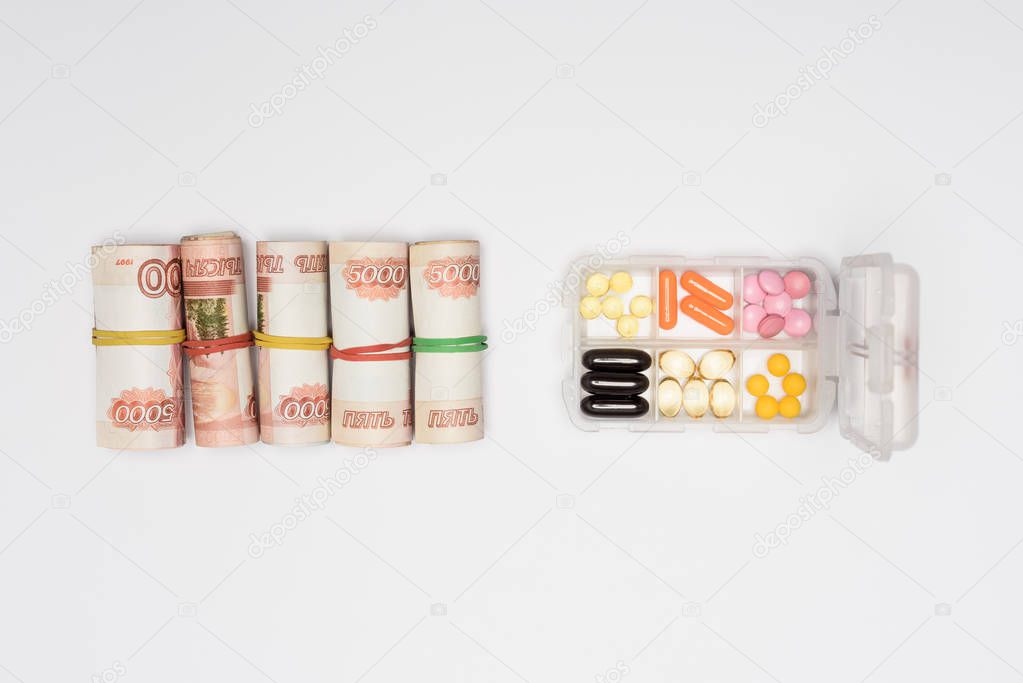 top view of money rolls and pills in plastic container isolated on grey