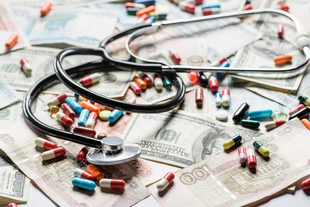 close up of multicolored pills and stethoscope on cash background