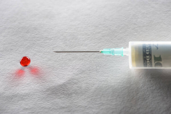 close up of syringe with money injection and red round pill on grey background