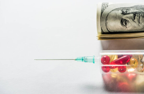 close up of syringe with medication near money roll on grey background 