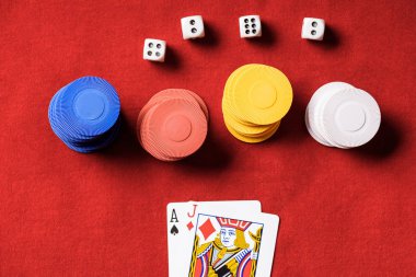 top view of red poker table with multicolored chips, dices and two unfolded cards