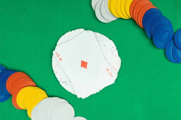 top view of green poker table with multicolored chips and playing card with diamonds suit on deck