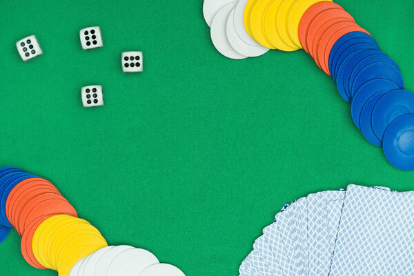 top view of green poker table and multicolored chips, dices, playing unfolded cards 