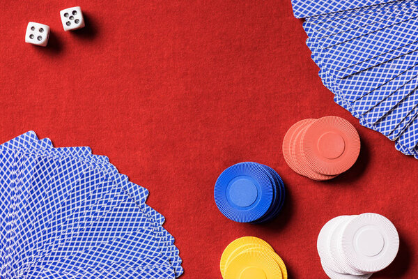 top view of red poker table with multicolored chips, dices and unfolded cards