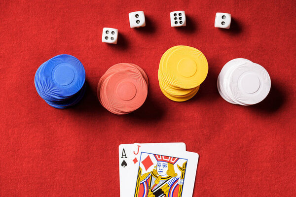 top view of red poker table with multicolored chips, dices and two unfolded cards