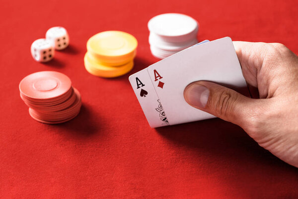 selective focus of man holding playing cards with chips and dices on background