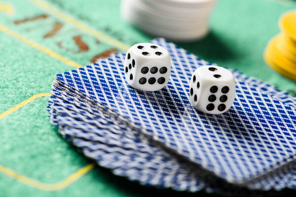 selective focus of dices on playing cards in deck with chips and green poker table on background