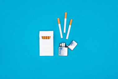 Top view of white cigarette pack and cigarette lighter isolated on blue clipart