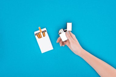 Partial view of woman holding cigarette lighter in hand isolated on blue clipart