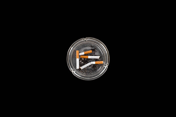 Top view of glass ashtray with ash and cigarettes isolated on black