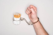 abgeschnittene Ansicht eines Mannes in Handschellen, der mit Zigaretten posiert, isoliert auf grauem, Nikotinabhängigkeitskonzept