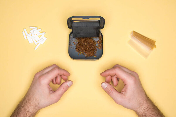 Частичное представление молодого человека, позирующего с табачной коробкой, изолированной на желтом
