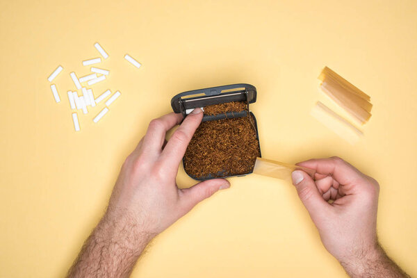 Обрезанный вид человека с табакеркой делая сигареты изолированы на желтый
