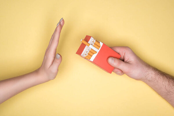 Cropped view of young woman refuses cigarettes isolated on yellow, stop smoking concept