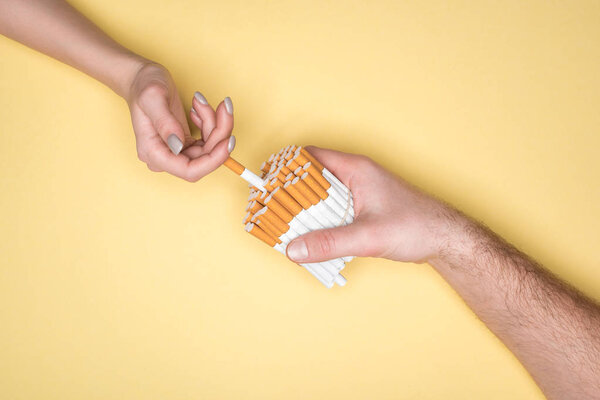 Cropped shot of woman and man holding cigarettes isolated on yellow