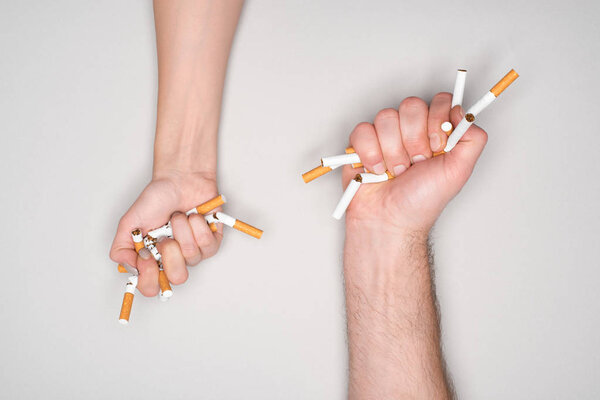 Partial view of woman and man breaking cigarettes isolated on grey, stop smoking concept