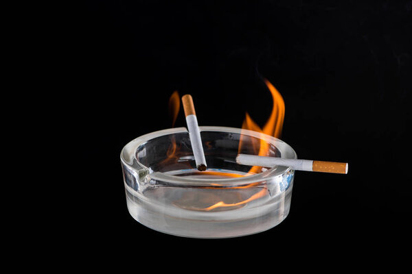 Studio view of glass ash-pot with burning cigarettes isolated on black