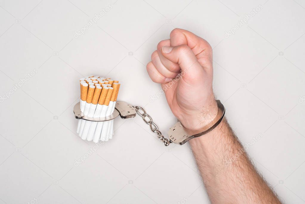 Cropped view of man in handcuffs posing with cigarettes isolated on grey, nicotine addiction concept