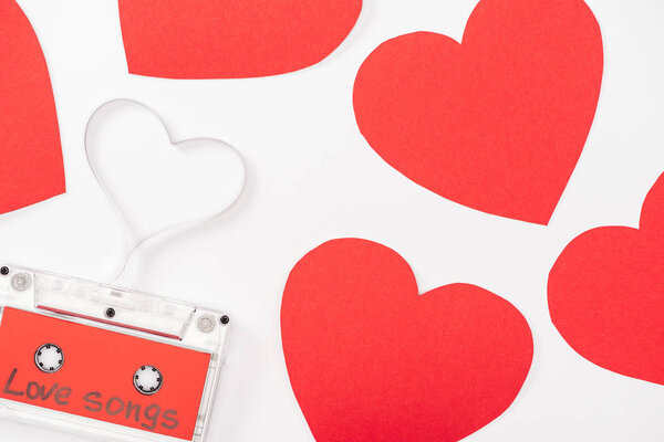top view of audio cassette with 'love songs' lettering and heart shaped cards isolated on white, st valentines day concept