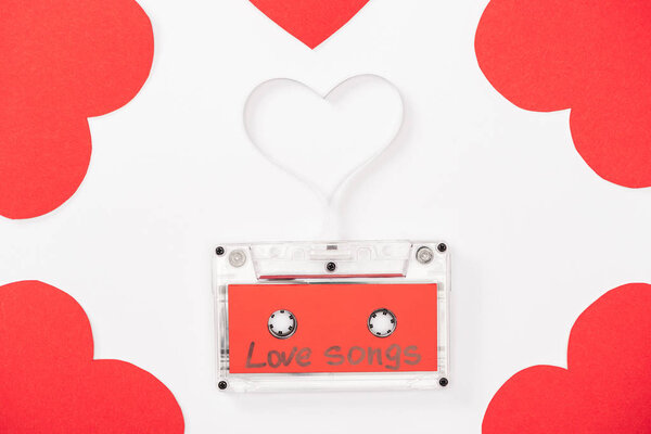 top view of audio cassette with 'love songs' lettering and heart shaped cards isolated on white, st valentines day concept