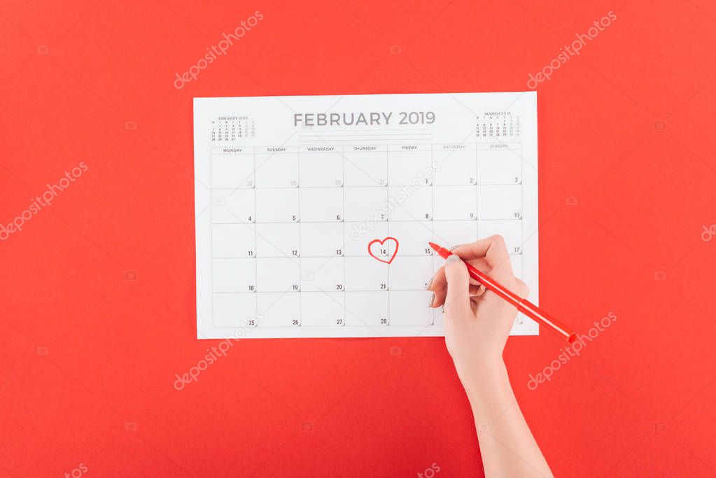 cropped view of woman holding marker over calendar with 14th february date marked isolated on red, st valentines day concept