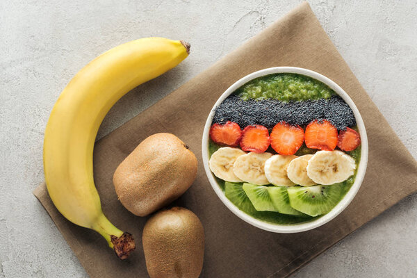 top view of delicious smoothie bowl with fresh fruits and ingredients on grey background