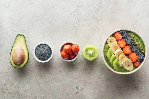 top view of healthy smoothie bowl with fresh fruits and ingredients on grey background