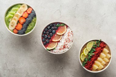 top view of healthy organic smoothie bowls with fruits on grey background clipart