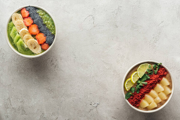 top view of healthy organic smoothie bowls with fruits on grey background with copy space