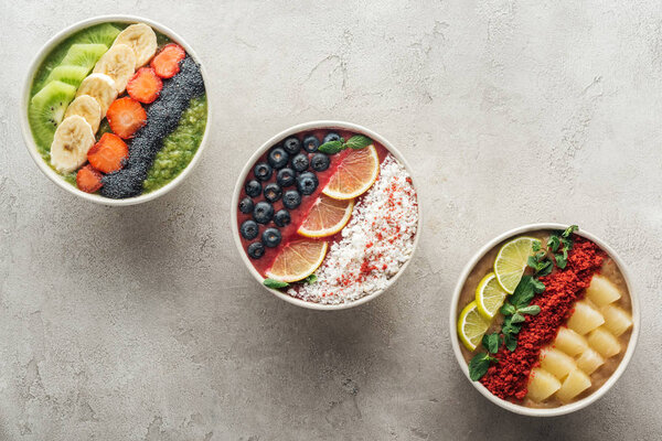 top view of healthy organic smoothie bowls with fruits on grey background
