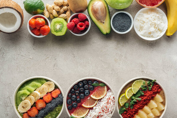 top view of smoothie bowls with ingredients on grey background