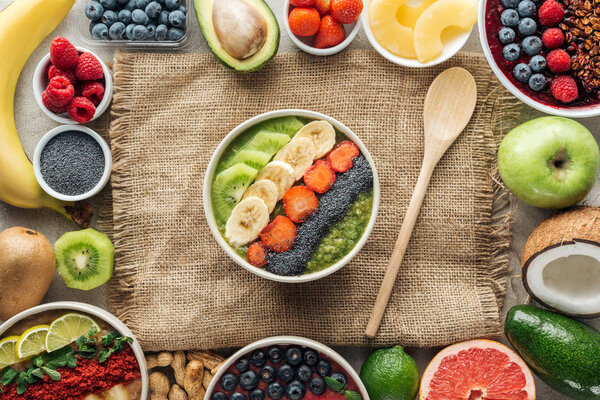 top view of smoothie bowls with wooden spoon and frame made of fresh ingredients on sackcloth