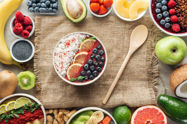 top view of smoothie bowls with wooden spoon and frame made of fresh ingredients on sackcloth
