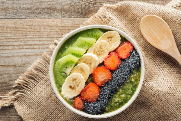 top view of fresh smoothie bowl on sackcloth and wooden background