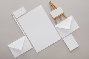 flat lay with white empty papers and letters with toy easel at workplace on grey background clipart